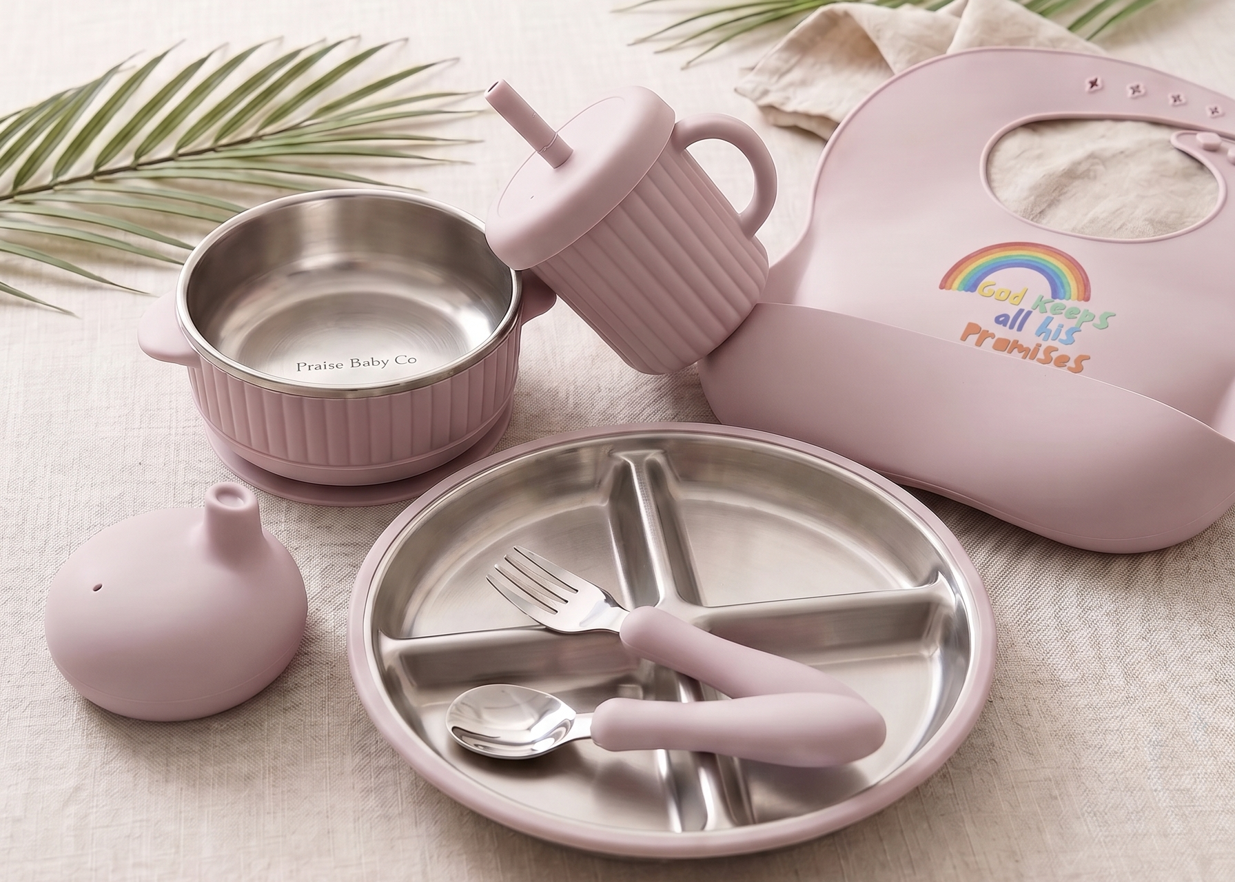Children's tableware set with pink silicone and stainless steel items. Bib featured a rainbow and words, God keeps all his promises.